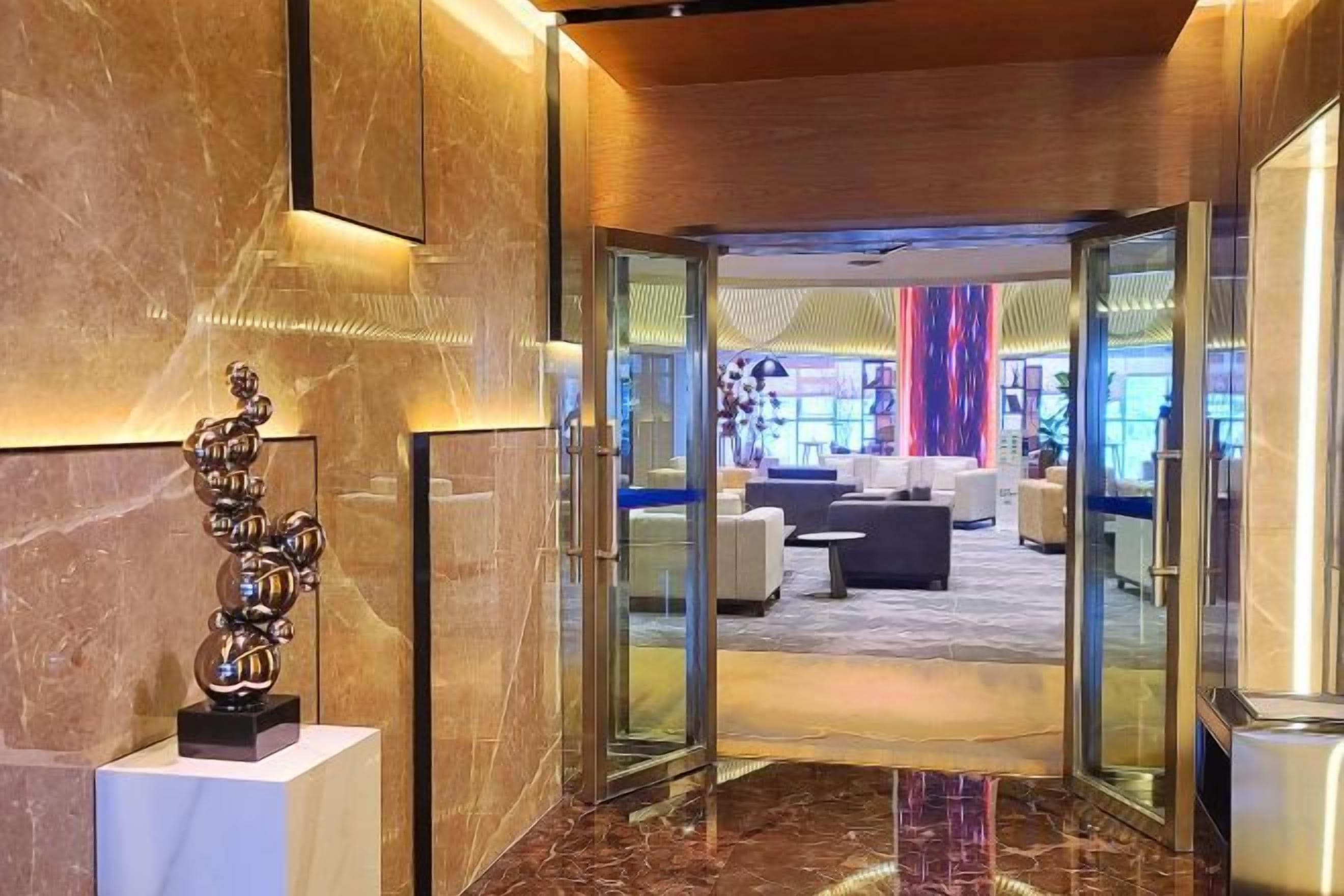 A modern lobby with a marble floor, a glass door entrance, and a seating area with sofas and a coffee table.