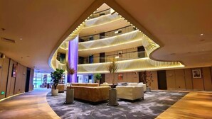 A modern hotel lobby with a curved wooden floor, a central seating area, and a multi-level atrium with glass railings.