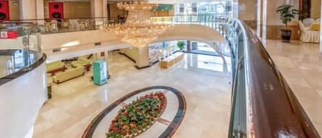 A spacious lobby with a central floral arrangement, a grand chandelier, and a curved glass railing overlooking the area.