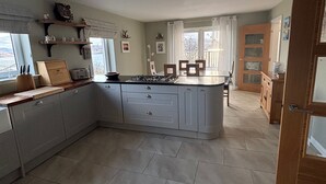 A spacious kitchen with grey cabinets, a central island, and a dining area with a view of the outdoors. - Mull Tranquility Retreat (Isle of Mull)