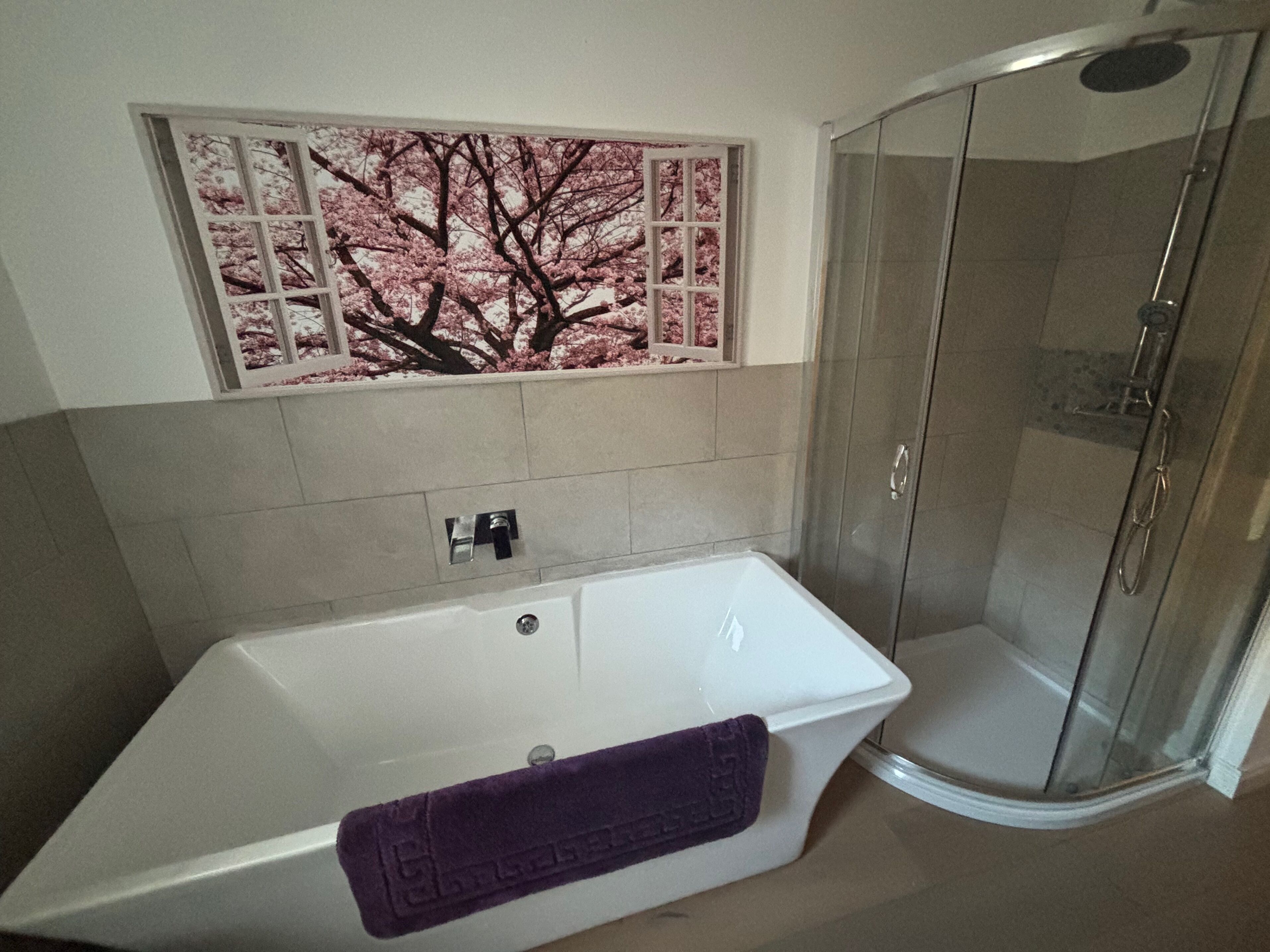 A bathroom with a white bathtub, a glass shower enclosure, and a decorative wall panel above the bathtub.