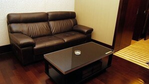 Un sofá de cuero marrón y una mesa de centro de vidrio negro en una habitación con piso de madera y pared con textura.