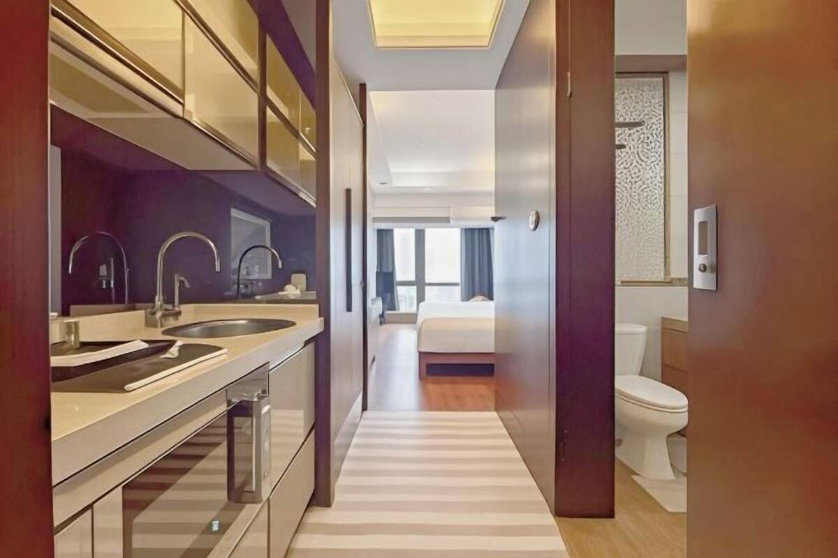 A modern hotel room with a kitchen area, a bed, and a bathroom.