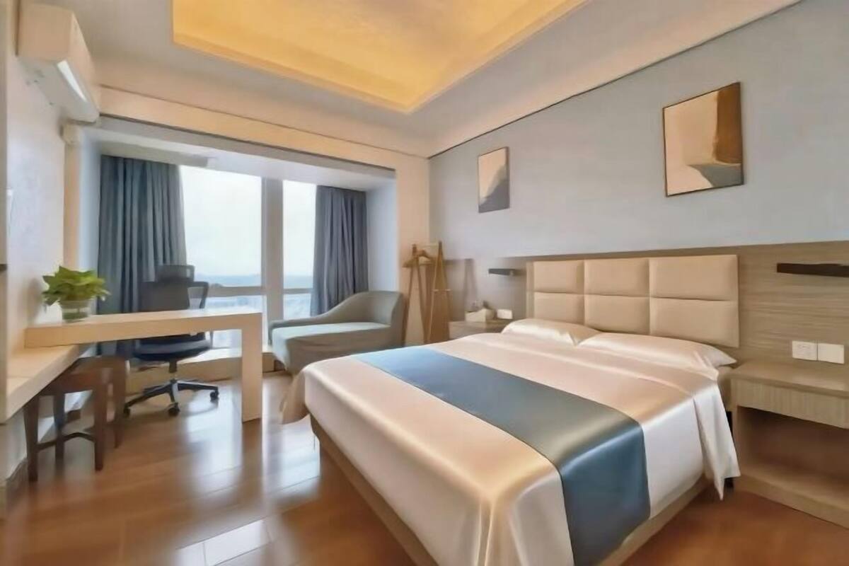 A hotel room with a bed, desk, chair, and large windows.