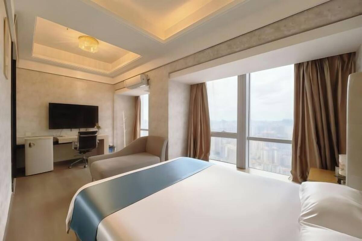 A hotel room with a large bed, a desk, a chair, a TV, and a city view.