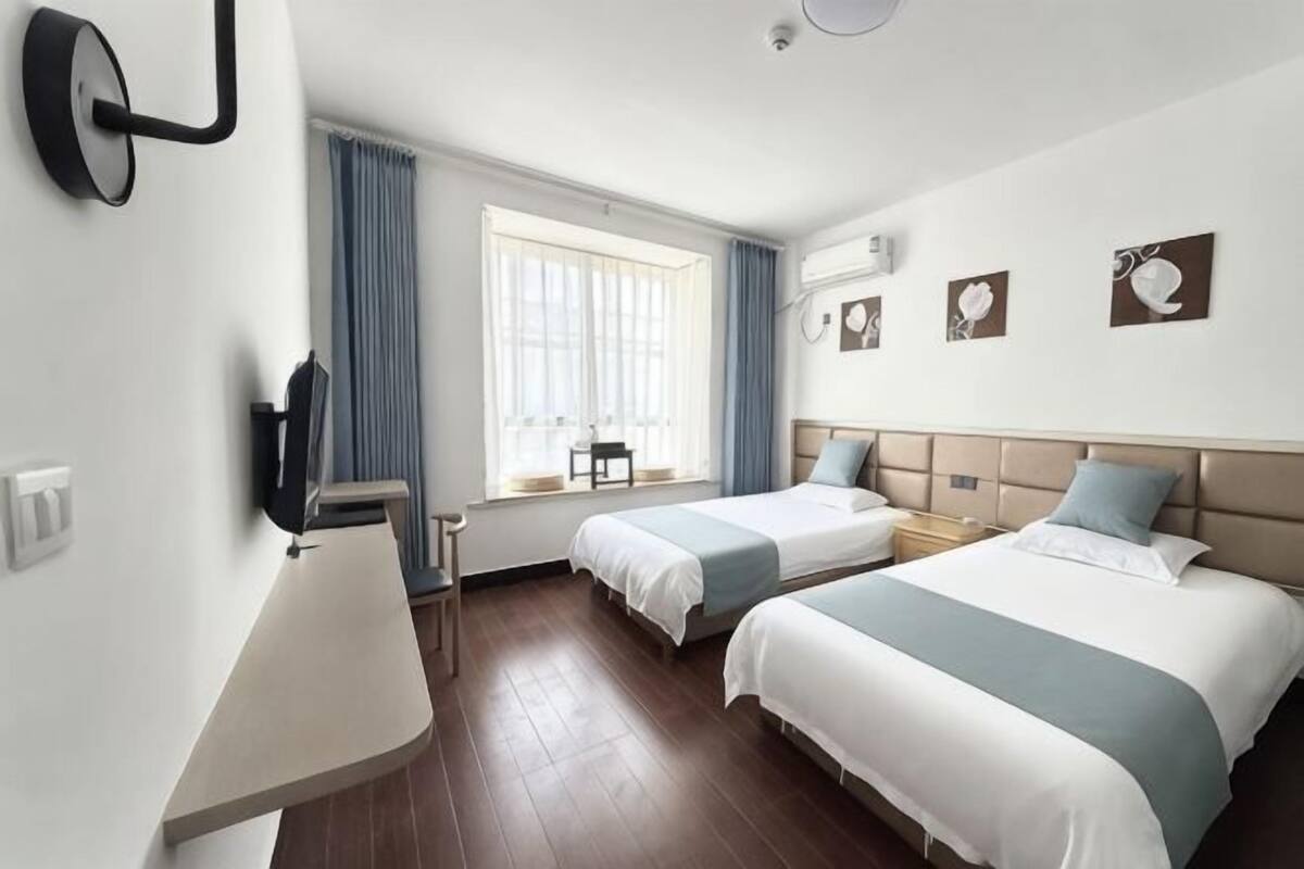 A hotel room with two beds, a desk, a chair, a window with curtains, and wall-mounted artwork.