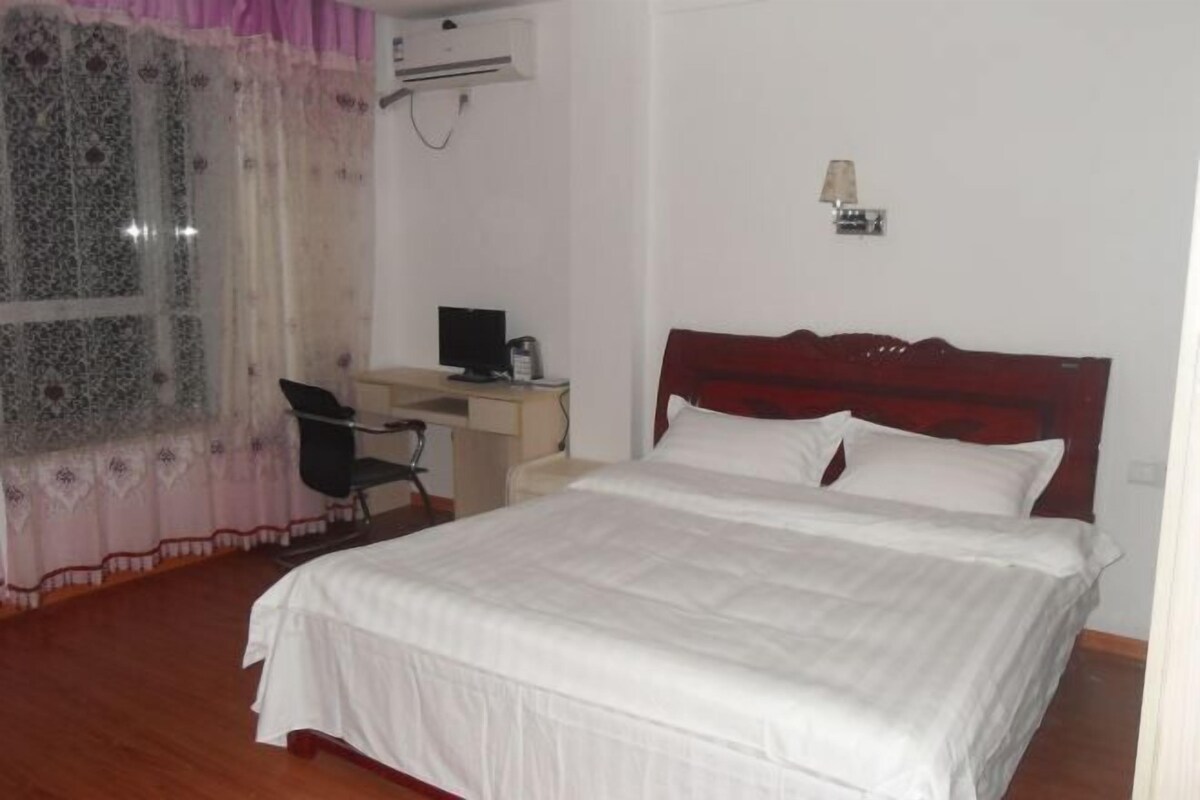 A bedroom with a bed, a desk with a computer, a chair, and a lamp.