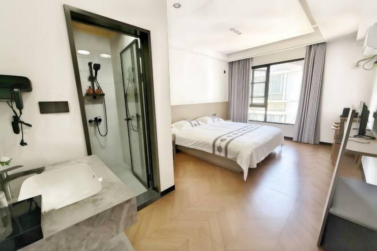 A hotel room with a bed, a shower area, a bathroom with a bathtub, and a desk with a chair.