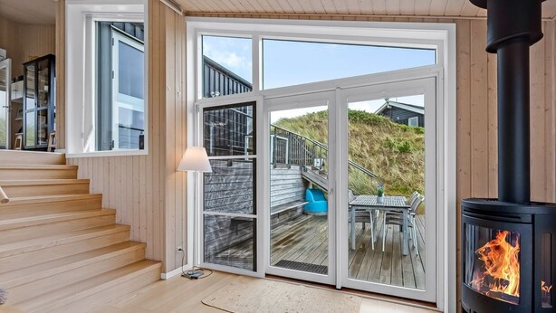 A modern interior with a wooden staircase, a glass door leading outside, and a wood-burning stove. - "Paaske" -  from the sea by Interhome (Ringkøbing)