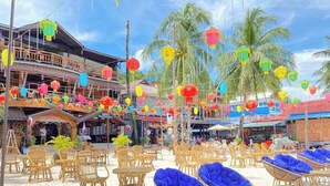 A beachside restaurant with wicker chairs and tables, palm trees, and colorful lanterns. - Green Ocean Lodge (Koh Rong)