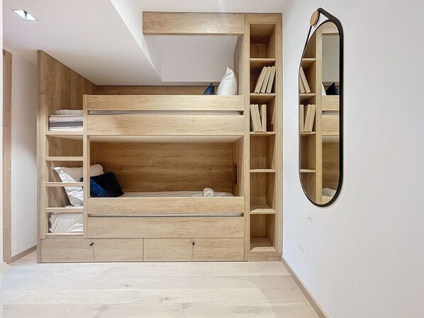 Een stapelbed met een houten afwerking, een ingebouwde boekenkast en een spiegel aan de muur.