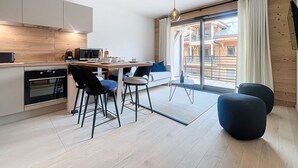 Une cuisine moderne avec un coin repas, un plancher en bois et une vue sur un bâtiment en bois, visible à travers de grandes fenêtres.