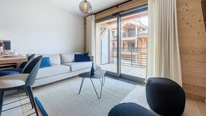 Un salon moderne avec un canapé, des fauteuils, une table basse et une grande fenêtre agrémentée de rideaux.