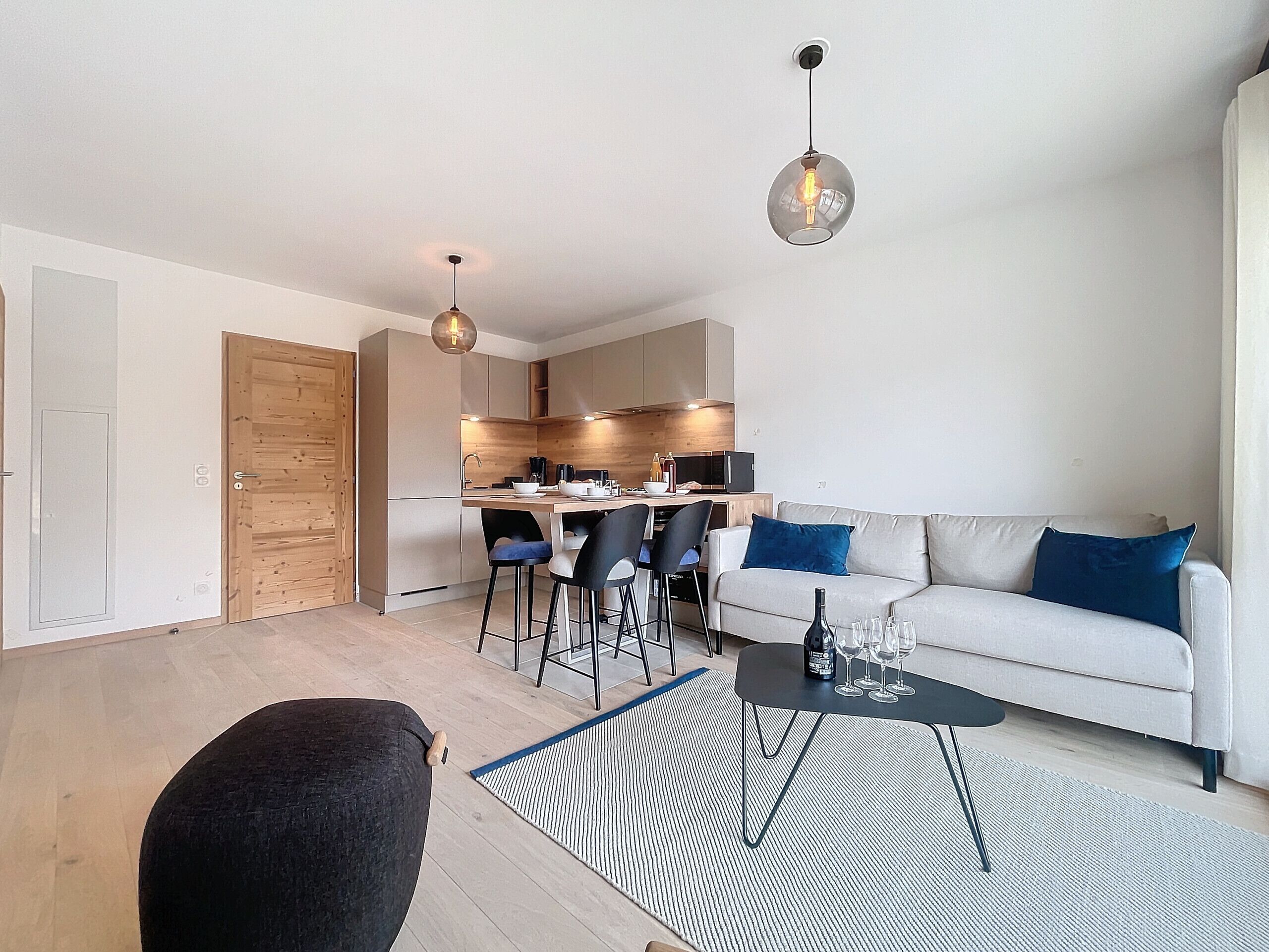 A modern living room with a sofa, coffee table, and chairs. There is a kitchen area with a dining table and chairs.