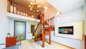 Un amplio salón con una escalera de madera, un televisor montado y un comedor.