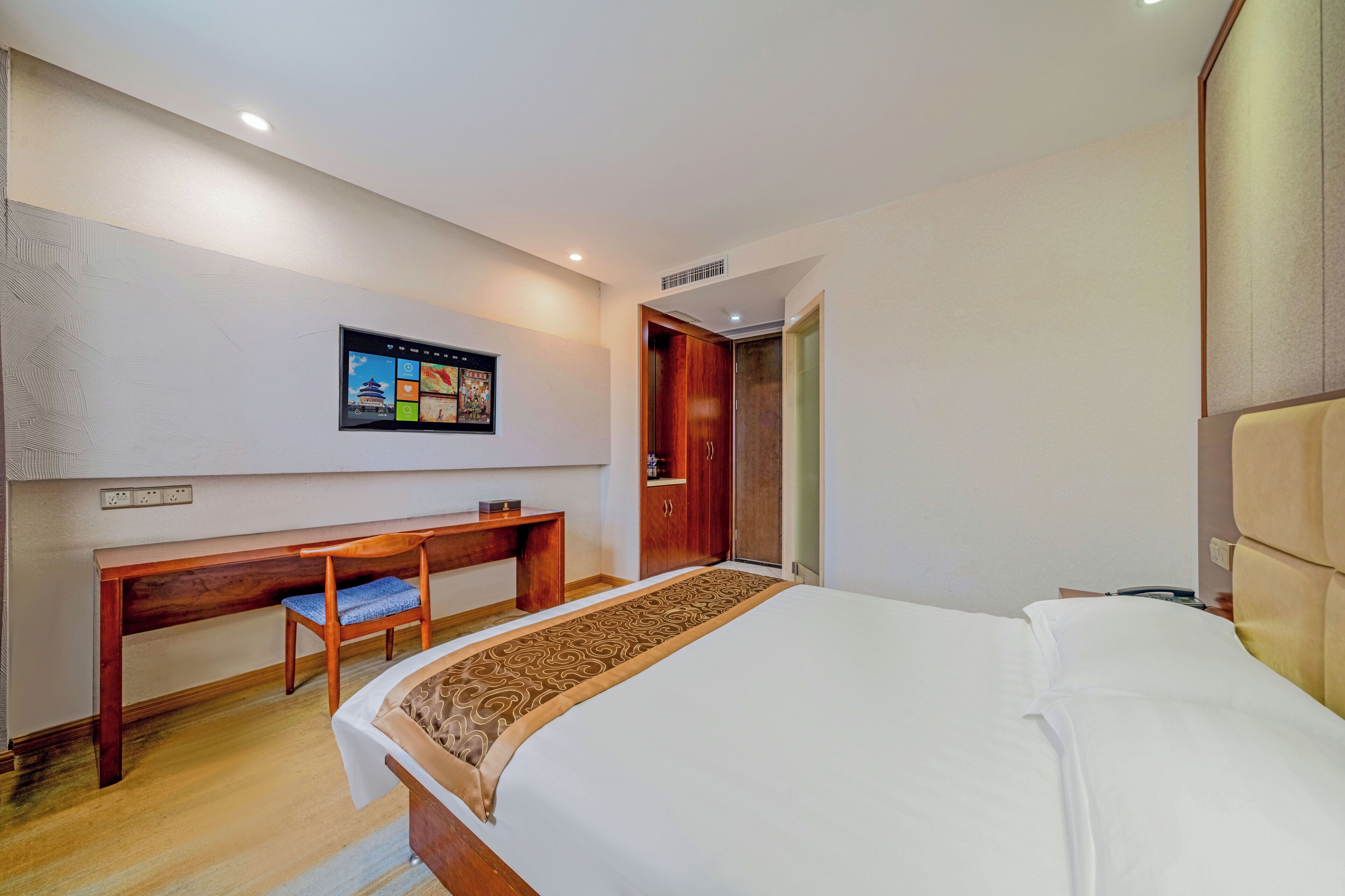 Ein Hotelzimmer mit einem großen Bett, einem Holztisch, einem Stuhl, einem an der Wand montierten Fernseher und einem Kleiderschrank.