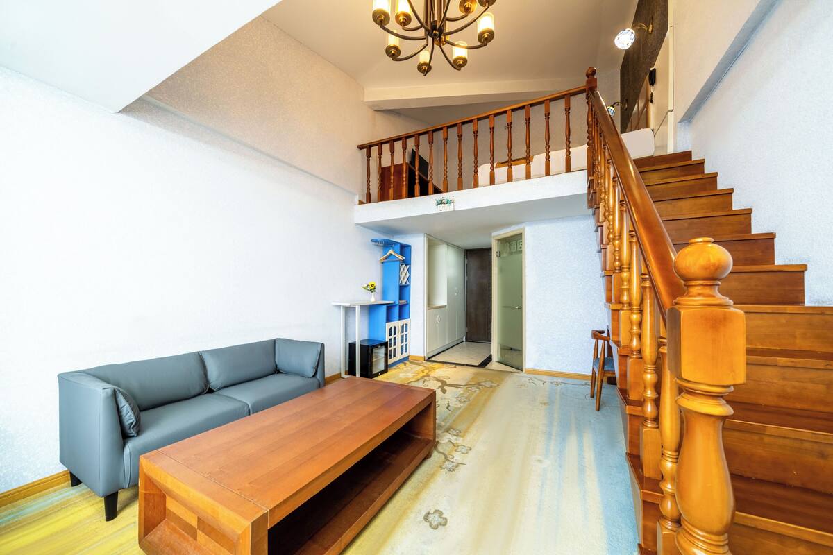 Ein Wohnzimmer mit einer Holztreppe, einem grauen Sofa und einem Holztisch.