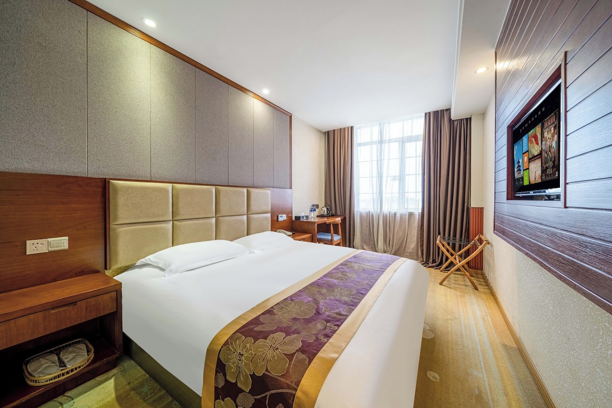 Ein Hotelzimmer mit einem großen Bett, einem Holzkopfende, einem an der Wand montierten Fernseher und einem Schreibtisch mit einem Stuhl.