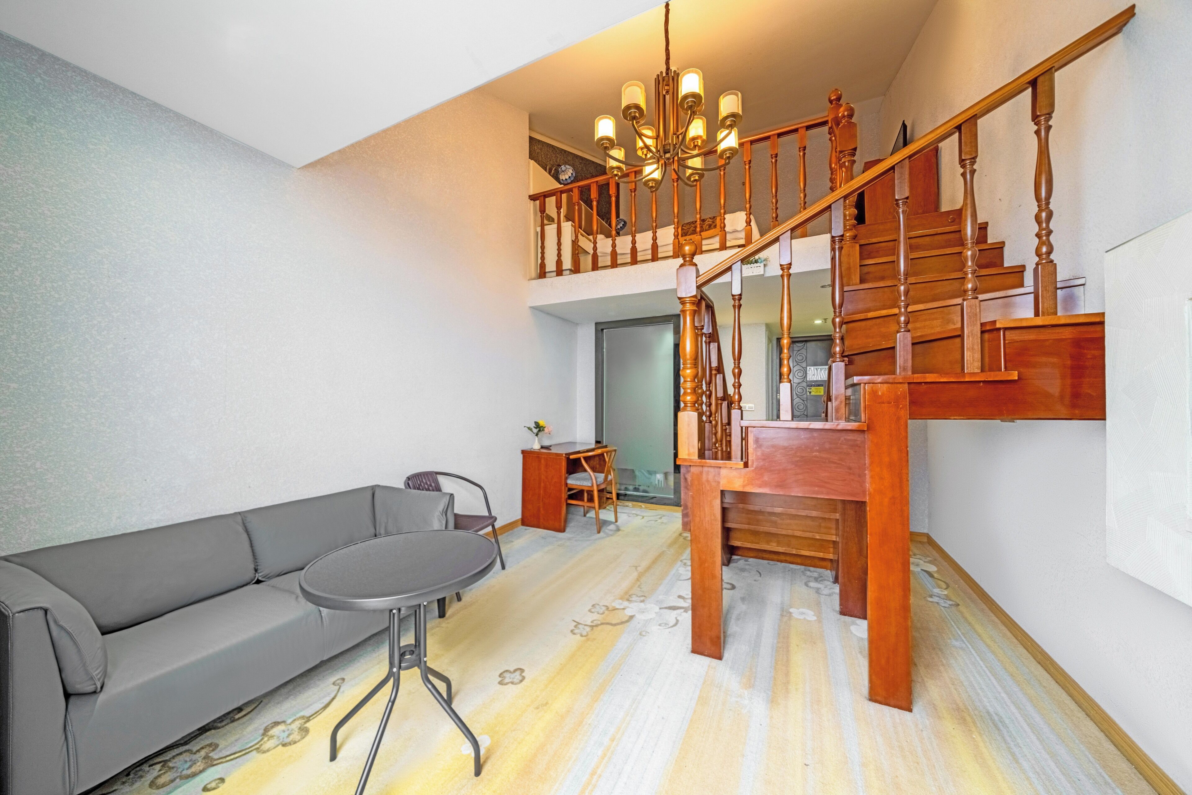 A spacious living area with a grey sofa, a round table, and a wooden staircase.