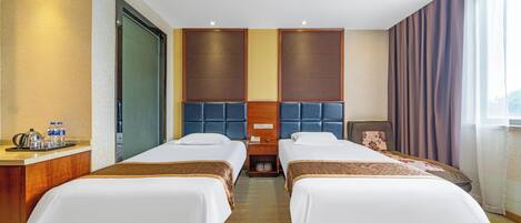 Habitación de hotel con dos camas, cabecero de madera, minibar y un ventanal con cortinas.