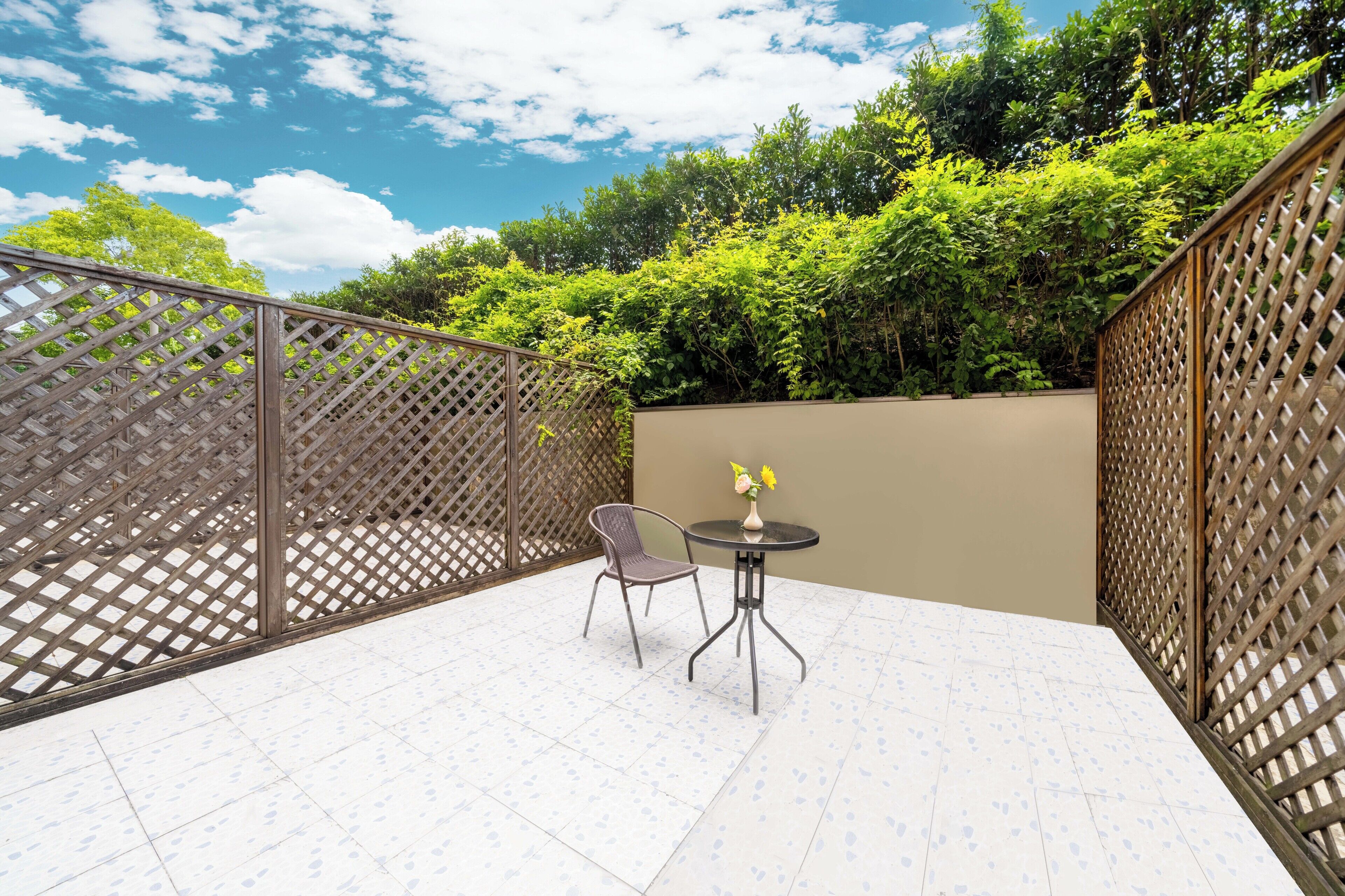 A patio with a table and chairs, surrounded by a wooden lattice fence, and a view of lush greenery.