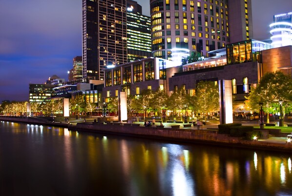 A waterfront hotel with modern architecture, a river in the foreground, and illuminated windows.