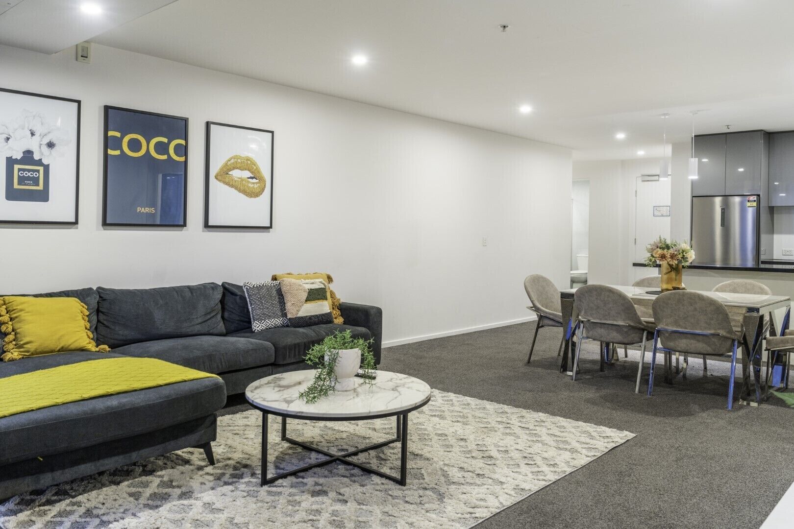 A modern living room with a grey sofa, a coffee table, and a dining area with chairs and a table.