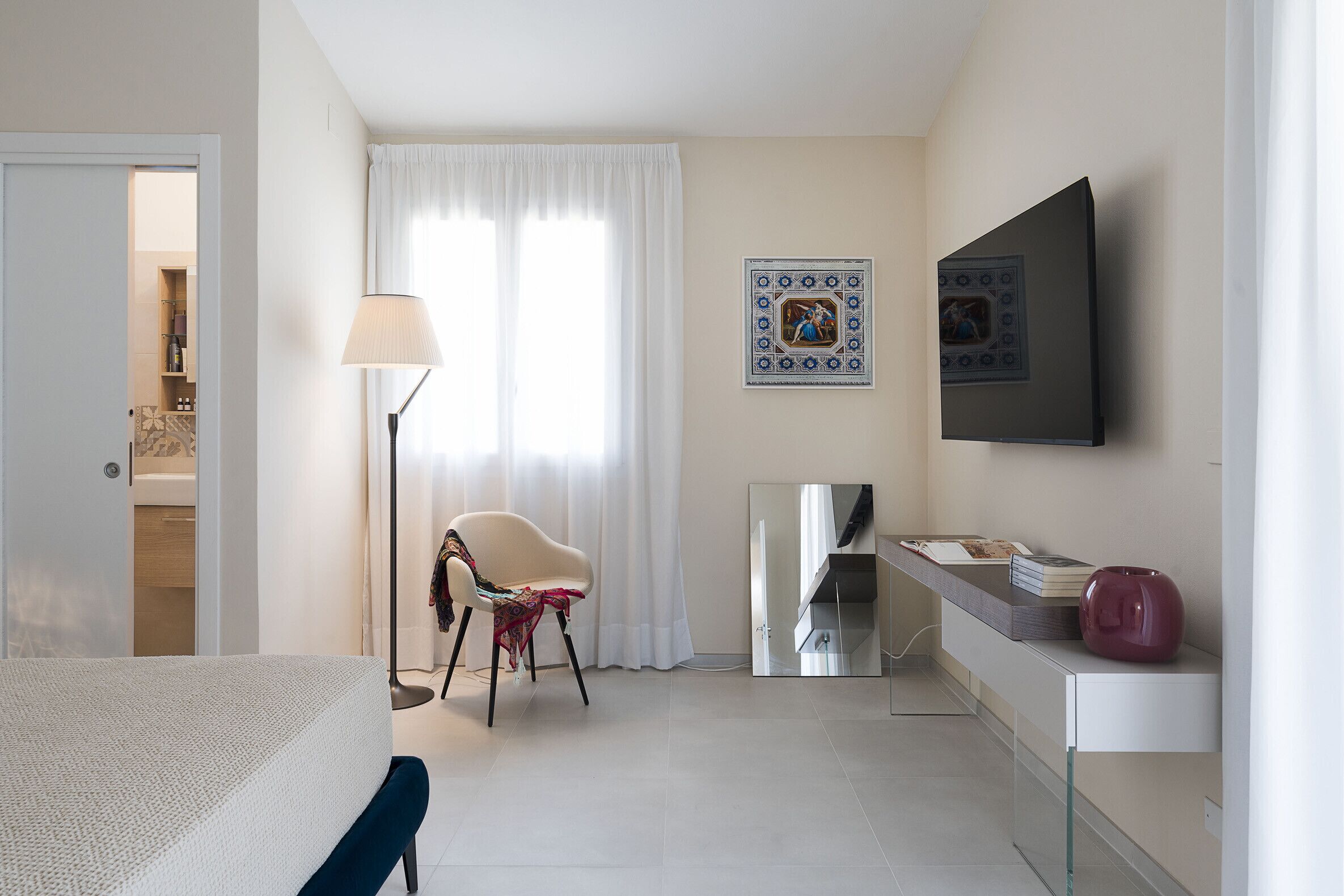 Una habitació d'hotel amb llit, cadira, escriptori, làmpada, mirall i televisió.