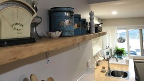 Eine Küche mit Holzregalen, die alte Küchenutensilien, eine Waage und ein Fenster mit Blick ins Freie beherbergen.