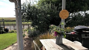 Eine Terrasse im Freien mit einem Holztisch, Stühlen, einem Grill und einem Holzschild mit Nummern.