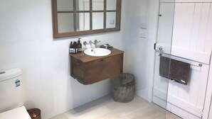 Ein Badezimmer mit Holz-Waschtisch, einer weißen Spüle, einem Spiegel und einer Duschkabine.