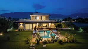 Une maison moderne à deux étages avec une piscine, entourée de jardins bien entretenus et offrant une vue sur les montagnes lointaines.