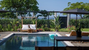Un espace piscine agrémenté de chaises longues et de parasols, entouré d’une végétation luxuriante et offrant une vue sur la mer.