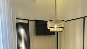 Un'area pranzo moderna con un tavolo rotondo in legno, quattro sedie, un lampadario in rattan sospeso, un televisore piatto a parete e una pianta in vaso.