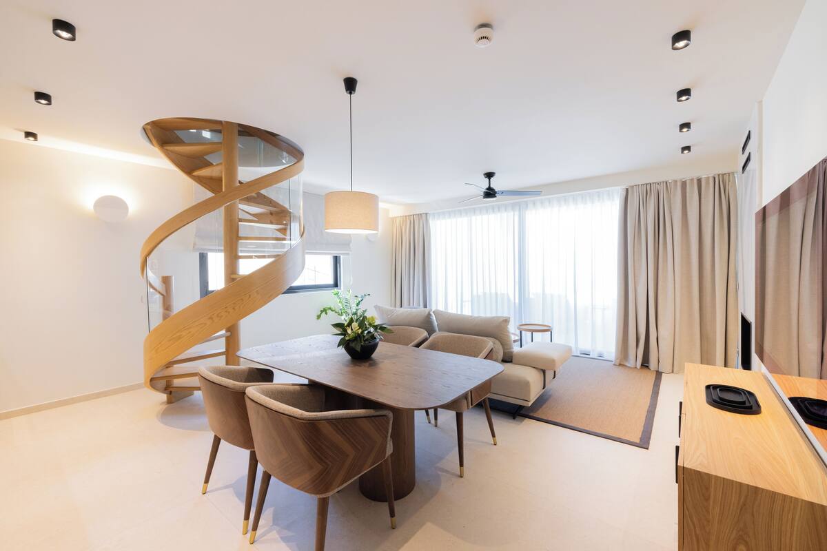 A modern living room with a spiral staircase, a dining area with a wooden table and chairs, a sofa, and a TV.