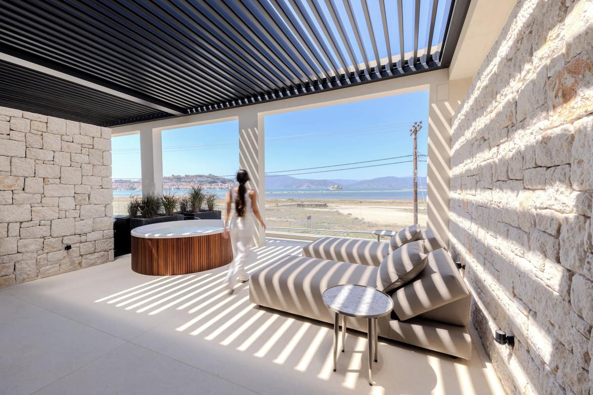 A modern outdoor lounge area with a stone wall, a wooden bench, and a sofa with striped cushions.