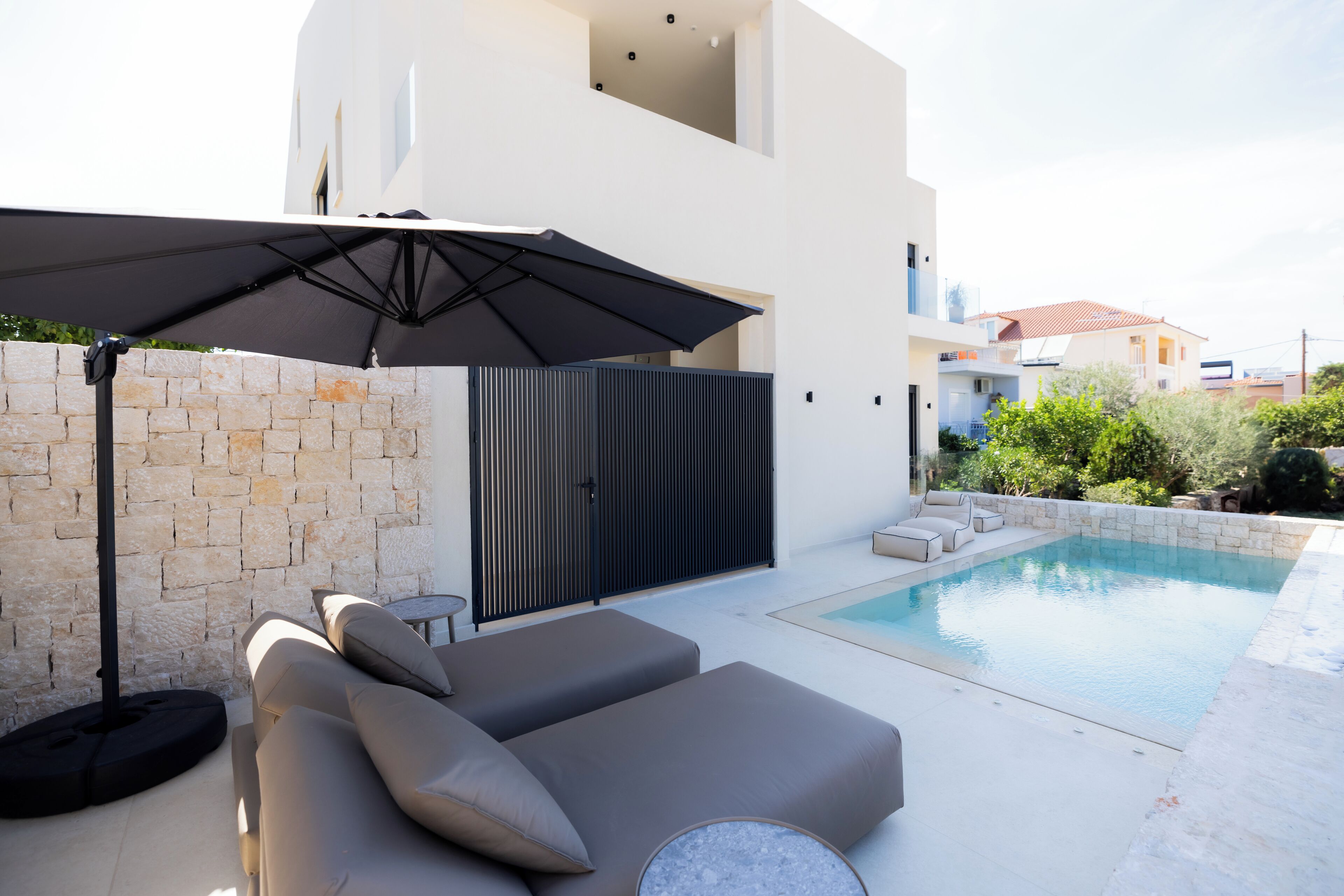 A modern outdoor pool area with a built-in seating area and a large umbrella providing shade.