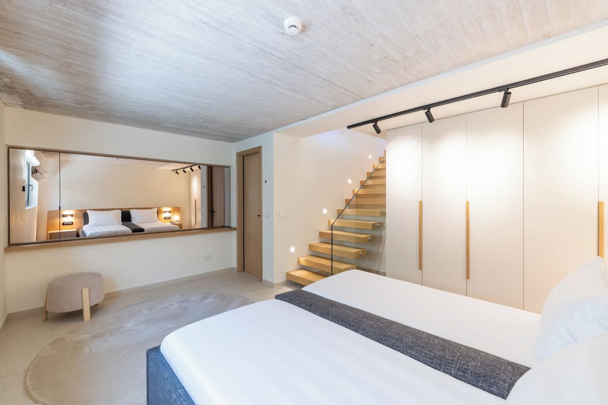 A modern bedroom with a large bed, a wooden staircase, and a wardrobe.