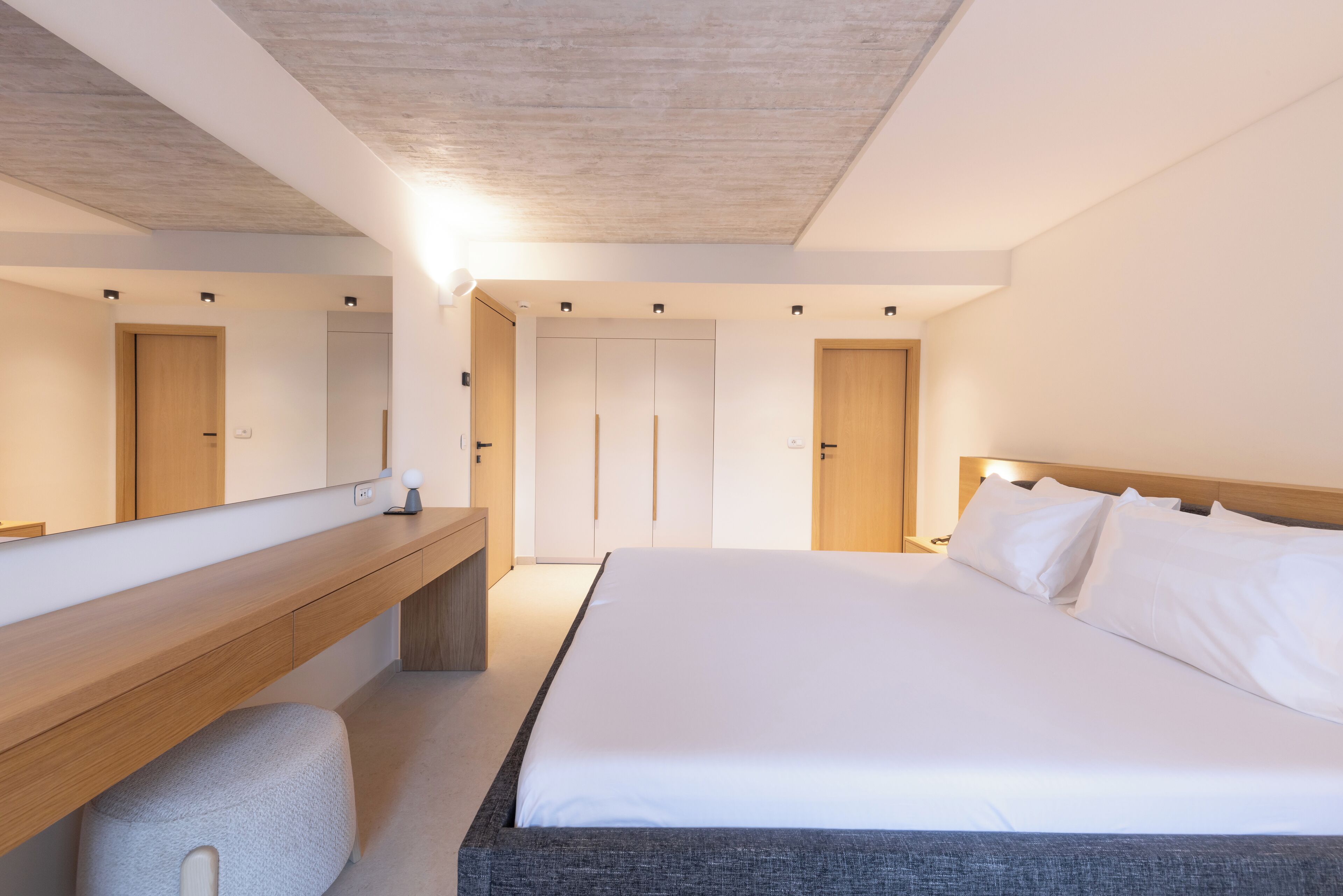 A modern bedroom with a large bed, a wooden bench, a mirror, and a wardrobe.