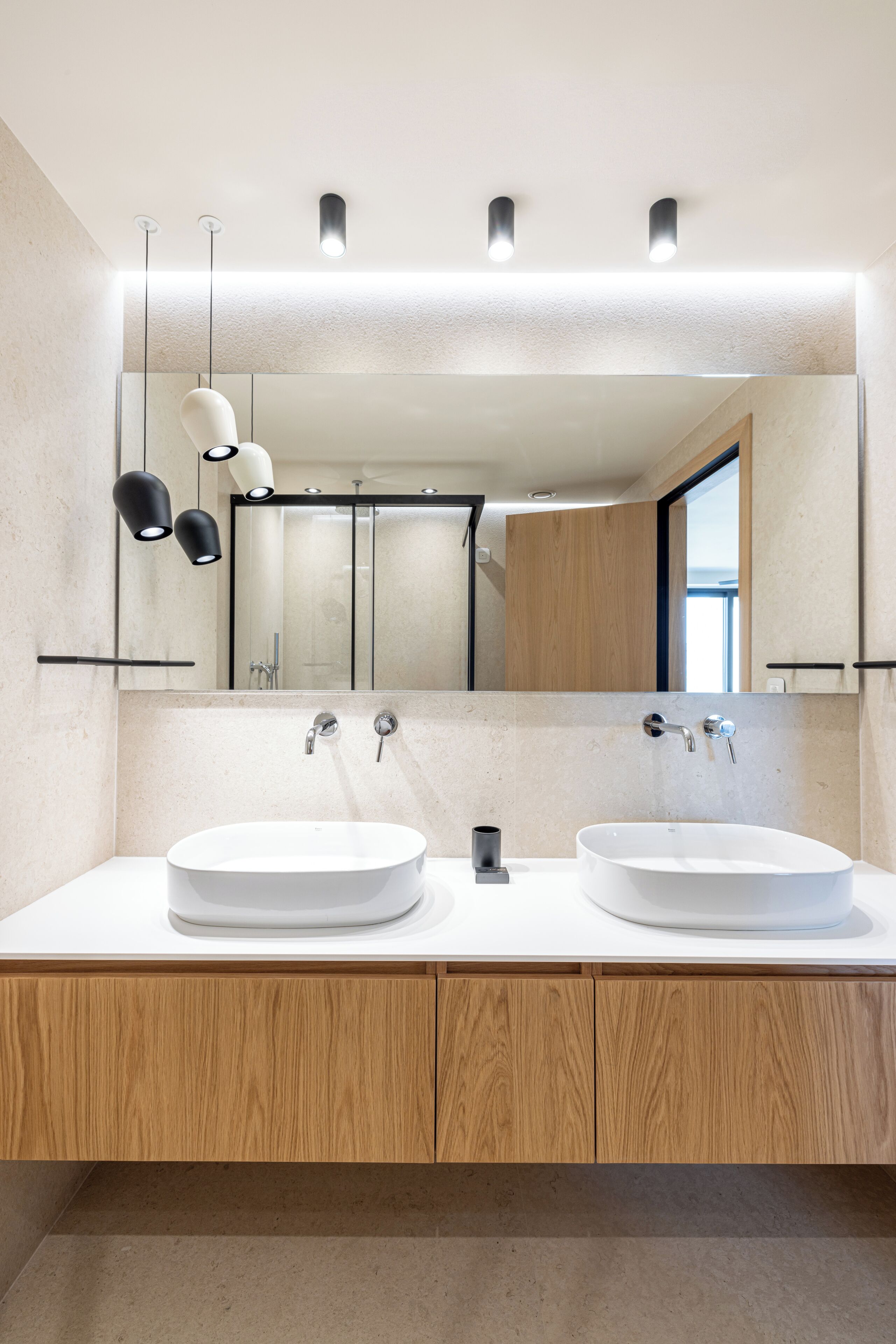 Ein modernes Badezimmer mit zwei Waschbecken, einem großen Spiegel und Pendelleuchten.