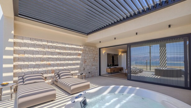 Ein moderner Außenbereich mit Whirlpool, Liegestühlen und einer Steinwand.