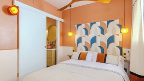 A hotel room with a bed, a large abstract wall art, a ceiling fan, and a bathroom visible through an open door.