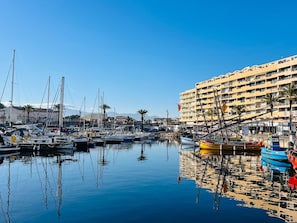 Puerto deportivo con barcos amarrados, un edificio con balcones y cielo despejado.