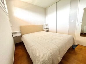 A bedroom with a bed, a nightstand, a wardrobe, and a mirror.