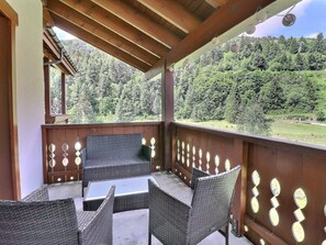 A covered outdoor seating area with wicker furniture and a view of a forested hillside. - Family apartment 3* 3 rooms, Méribel, near Lake Tuéda (Méribel)