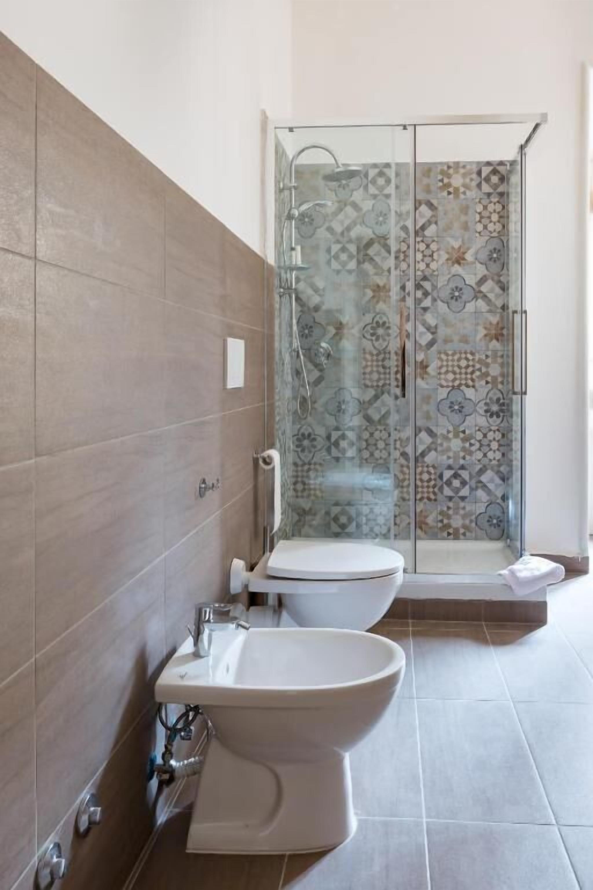 A bathroom with a toilet, bidet, and glass-enclosed shower.