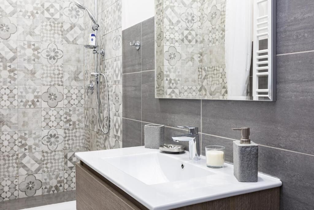 A modern bathroom with a large sink, a mirror, a shower, and patterned tiles.