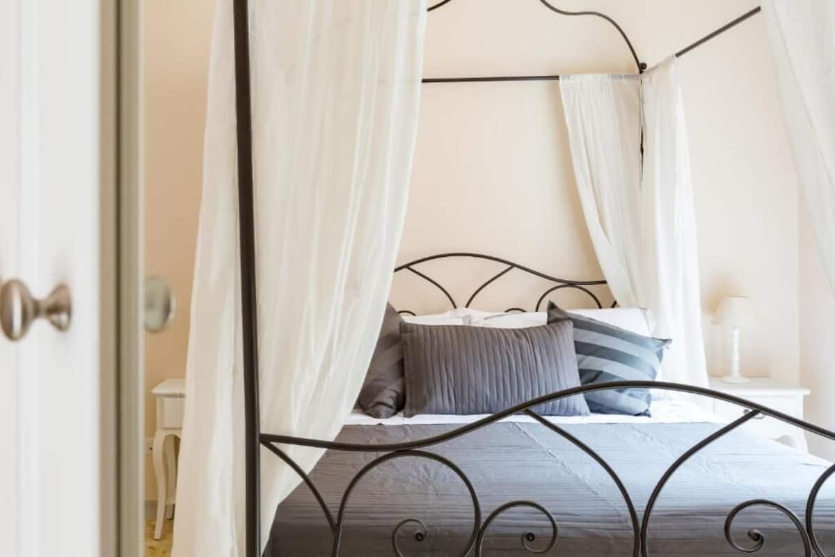 A bed with a metal frame, white curtains, and a bedside table with a lamp.