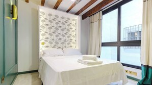 A neatly made bed with white linens, a patterned wall behind it, and a window with curtains. - Refined Studio Historic Center Alicante (Alicante)