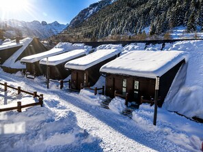 A row of wooden cabins with snow-covered roofs, set against a backdrop of snow-covered mountains and a clear sky. - BAQUEIRA URBANIZAC RUDA BLANHIBLAR APARTMENT FOR UP TO 7 PEOPLE (Baqueira)